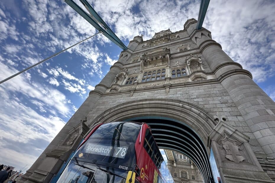 Roter Doppeldeckerbus fährt unter der Tower Bridge in London hindurch.