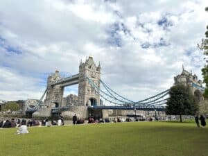 Tower Bridge in London with its iconic towers and suspension cables under a cloudy sky.