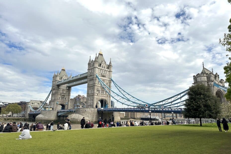 Tower Bridge in London with its iconic towers and suspension cables under a cloudy sky.
