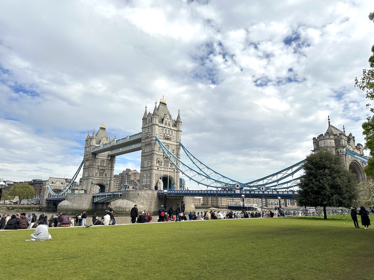 Tower Bridge in London with its iconic towers and suspension cables under a cloudy sky.