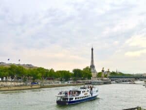 Ein Boot fährt auf der Seine mit dem Eiffelturm und Bäumen im Hintergrund.