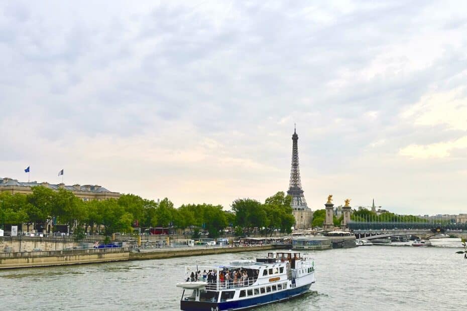 Ein Boot fährt auf der Seine mit dem Eiffelturm und Bäumen im Hintergrund.