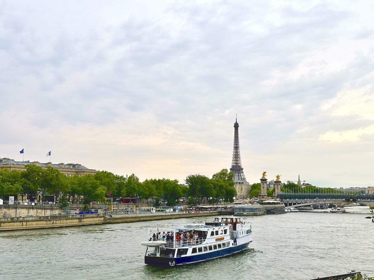 Ein Boot fährt auf der Seine mit dem Eiffelturm und Bäumen im Hintergrund.