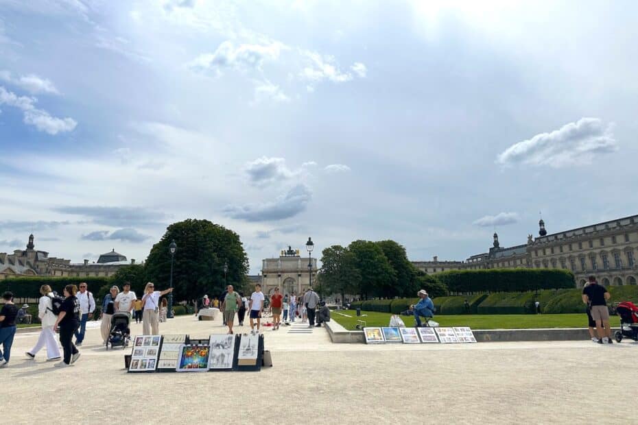 Menschen gehen durch einen Park mit Kunstwerken, die auf dem Boden ausgestellt sind, unter einem bewölkten Himmel.