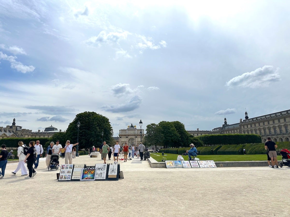 Menschen gehen durch einen Park mit Kunstwerken, die auf dem Boden ausgestellt sind, unter einem bewölkten Himmel.