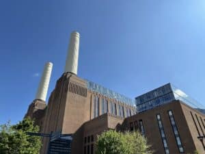 Battersea Power Station with its iconic chimneys and modern glass extensions against a blue sky.