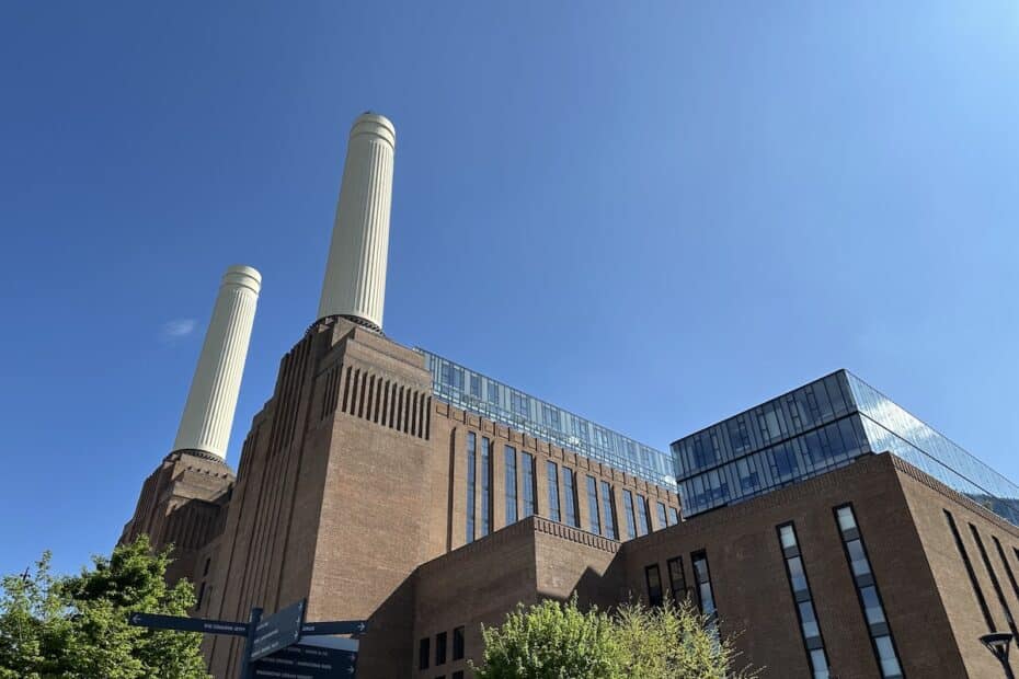 Battersea Power Station with its iconic chimneys and modern glass extensions against a blue sky.
