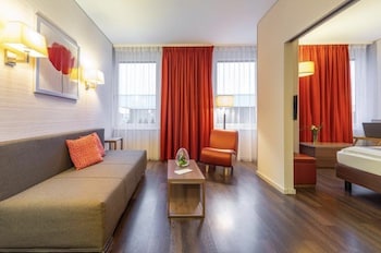 Ein modernes Hotelzimmer mit einem Sofa, einem Stuhl und einem Tisch in warmen Farbtönen.