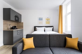 Ein modernes Zimmer mit einer Küchenzeile, einem Doppelbett und einem grauen Sofa mit gelben Kissen.