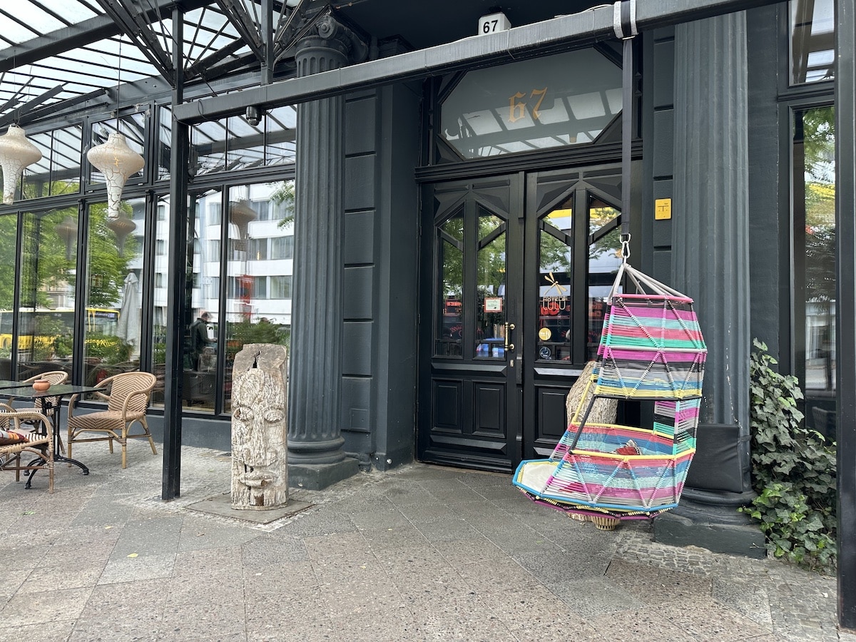 Bunte Hängesitzgelegenheit aus geflochtenem Material hängt vor einem Restaurant mit schwarzer Tür.