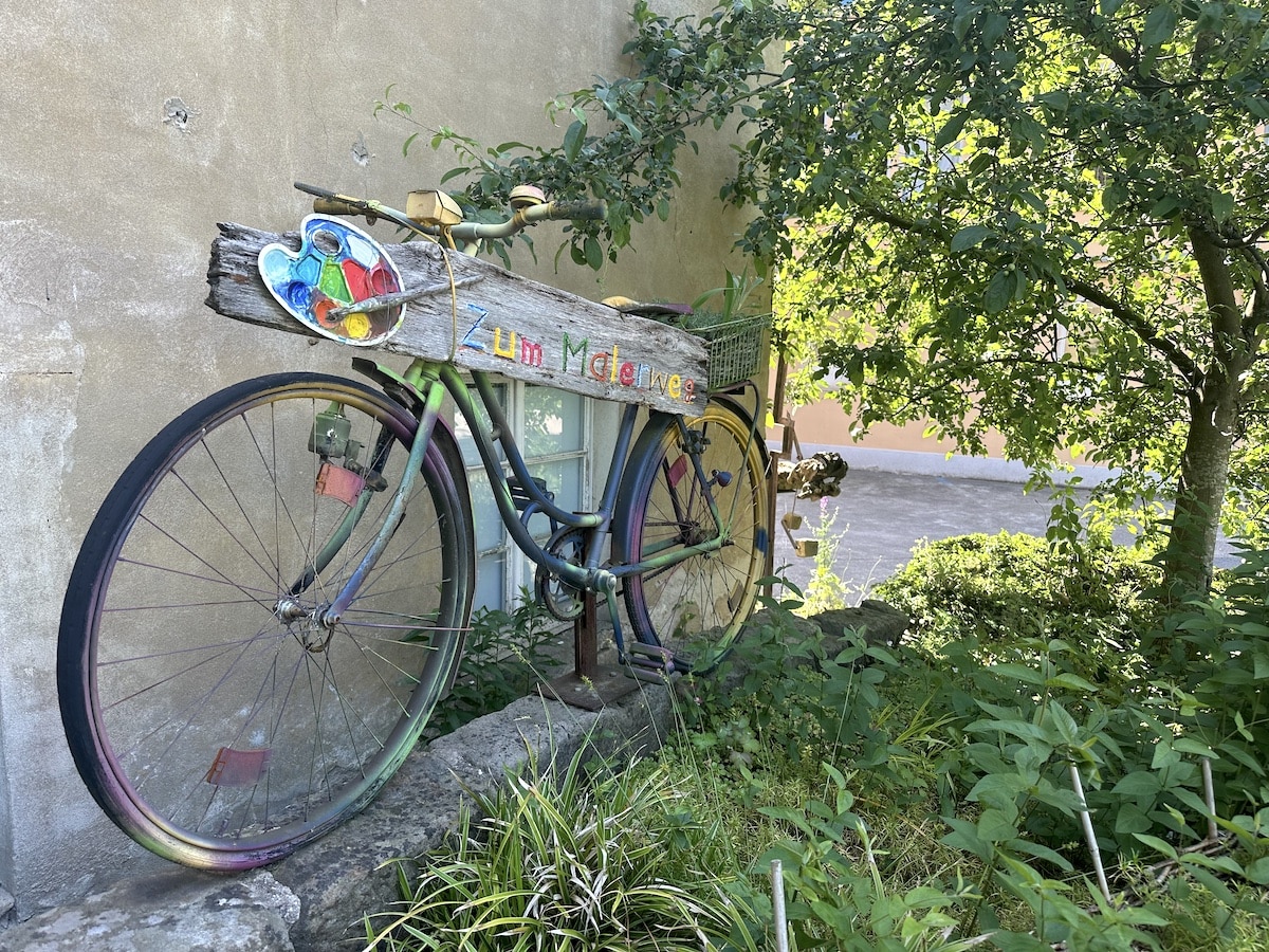 Buntes Fahrrad mit Holzschild und Pflanzen im Hintergrund, das als Dekoration dient.