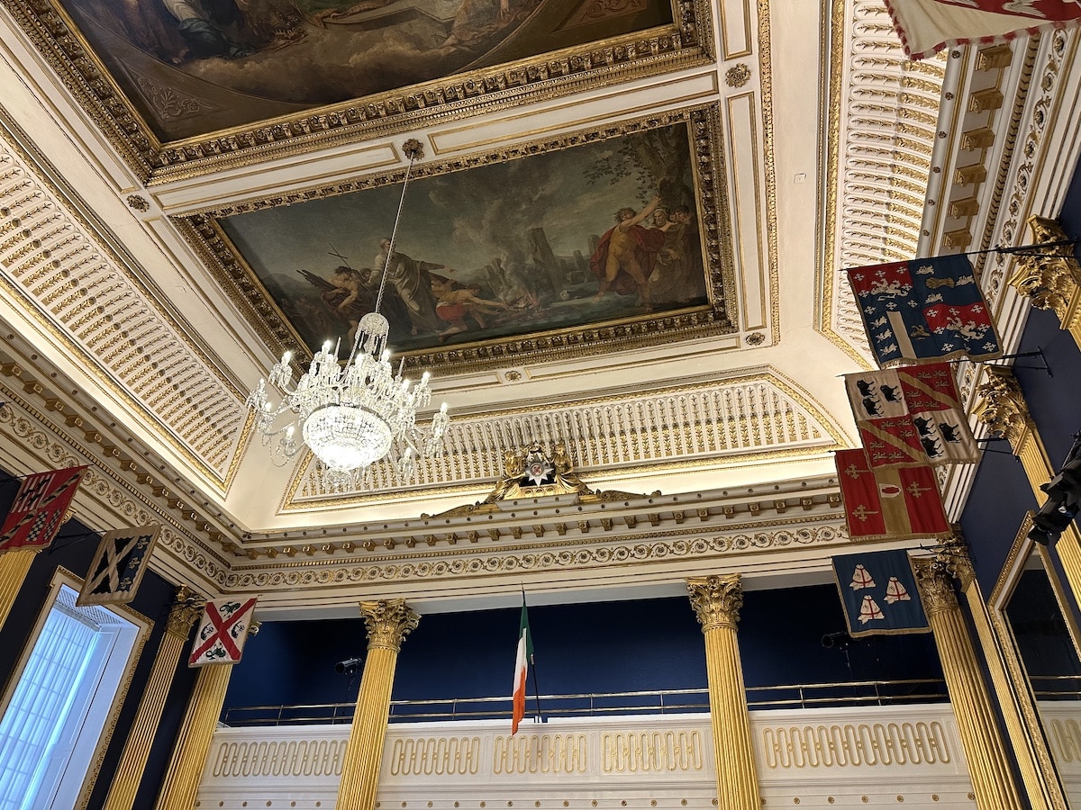 Innenansicht eines Raumes mit einem Kronleuchter und historischen Wandgemälden an der Decke.