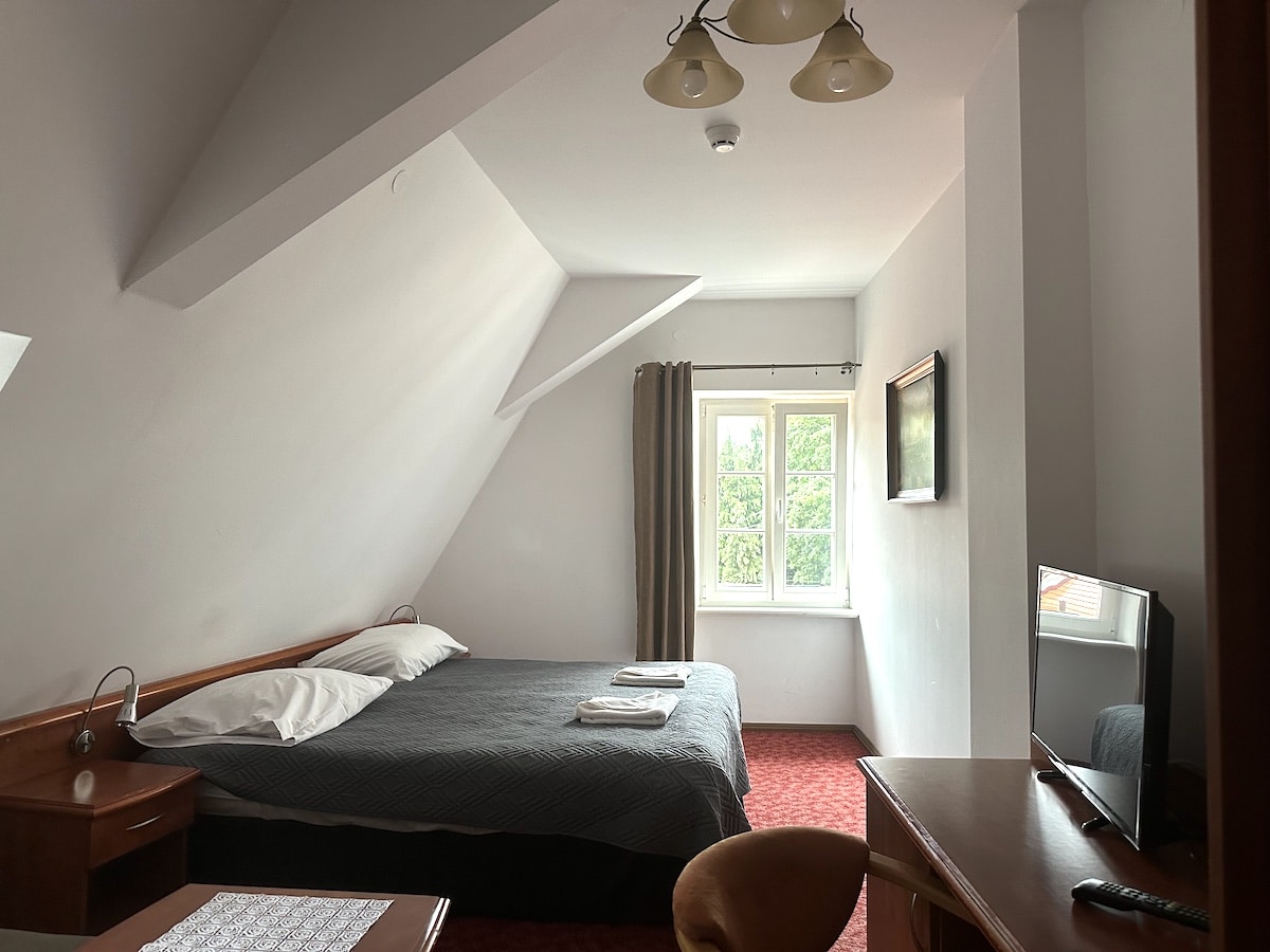 Ein Hotelzimmer mit einem Doppelbett, einem Fernseher und einem Tisch im Vordergrund.