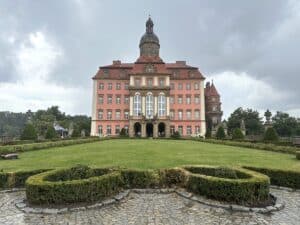 Historisches Schloss mit rosa Fassade und gepflegtem Garten im Vordergrund.