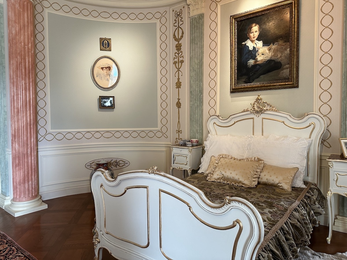 Ein elegantes Schlafzimmer mit einem antiken Bett, Kissen und Kunstwerken an der Wand.