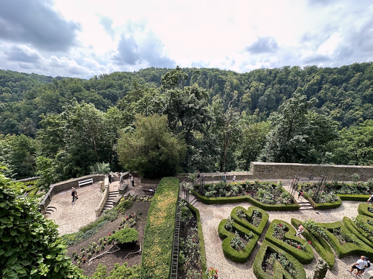Garten mit geometrischen Hecken und Blumenbeeten in einer Landschaft mit Bäumen im Hintergrund.