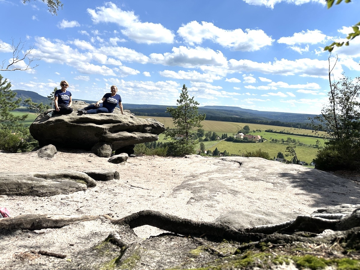 Zwei Personen sitzen auf einem großen Felsen in einer natürlichen Umgebung mit Blick auf die Landschaft.