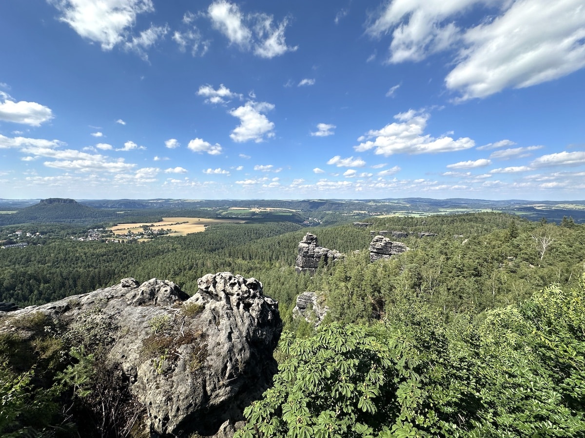 Panoramablick auf eine bewaldete Landschaft mit Felsen und Hügeln unter einem blauen Himmel mit Wolken.