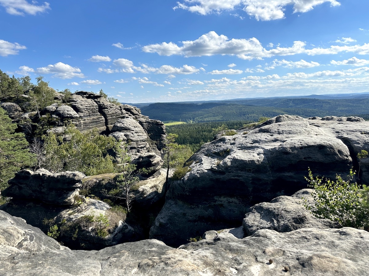 Felsenlandschaft mit großen Steinen und Bäumen unter einem blauen Himmel mit Wolken.