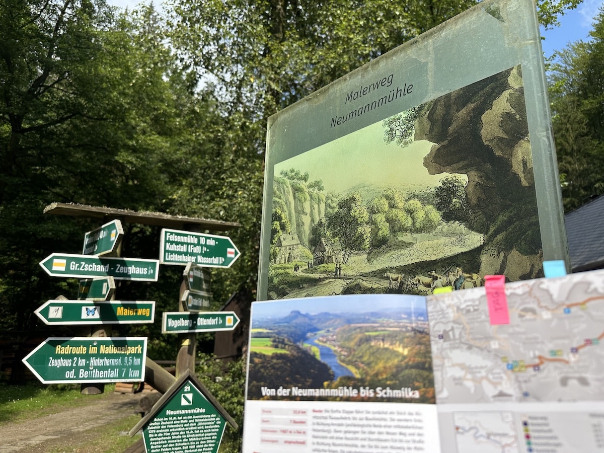 Wegweiser mit verschiedenen Richtungspunkten und einem Informationsschild über den Malerweg Neumannmühle.