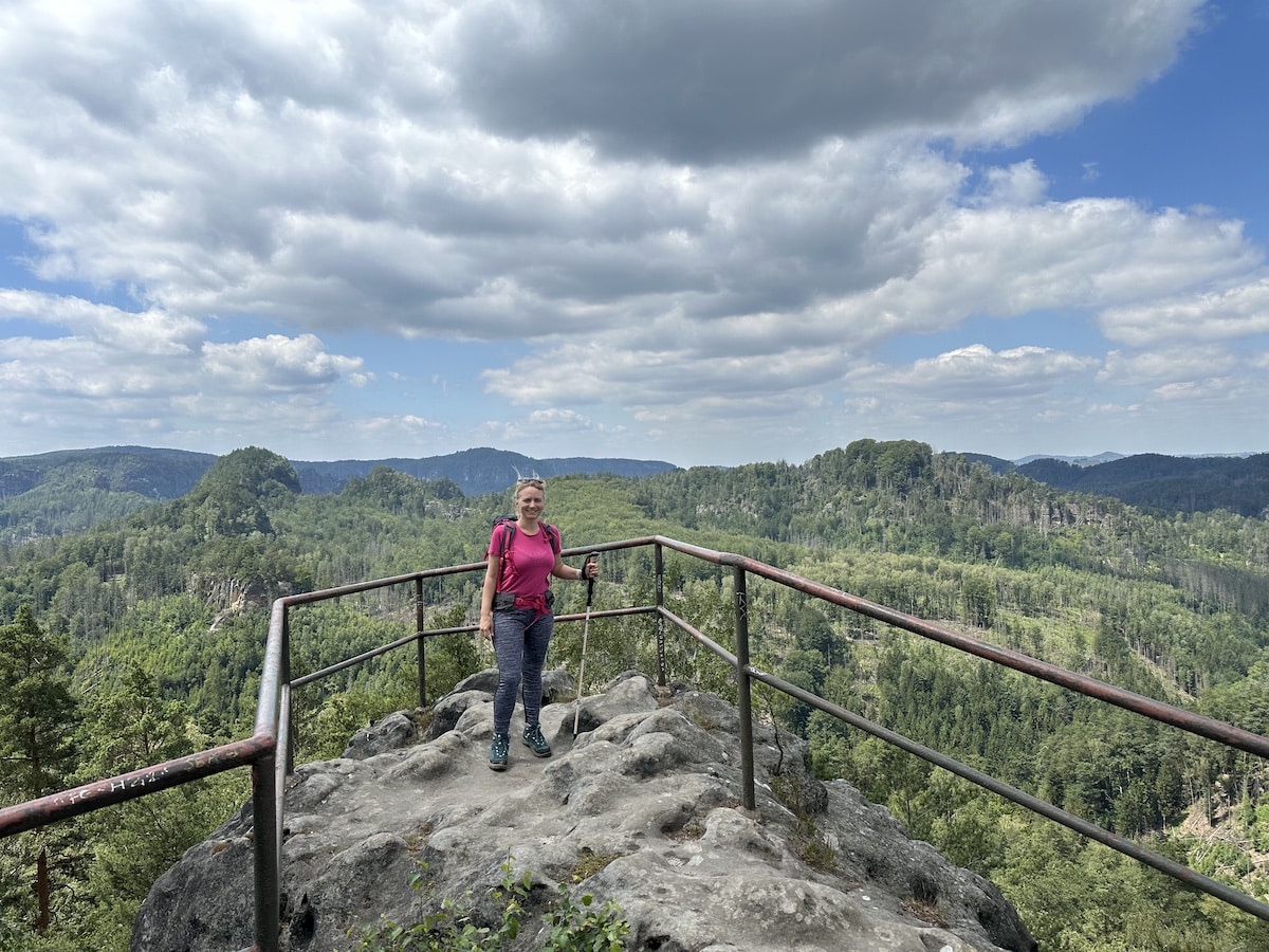 Eine Frau steht auf einer Aussichtsplattform mit Blick auf eine bewaldete Landschaft und den Himmel.