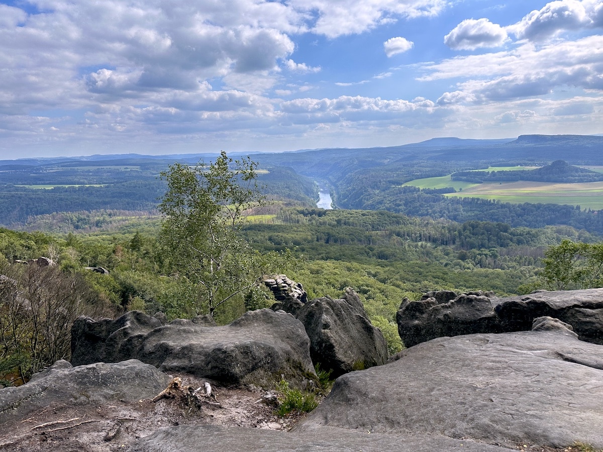 Blick auf ein Tal mit einem Fluss, umgeben von bewaldeten Hügeln und Felsen.