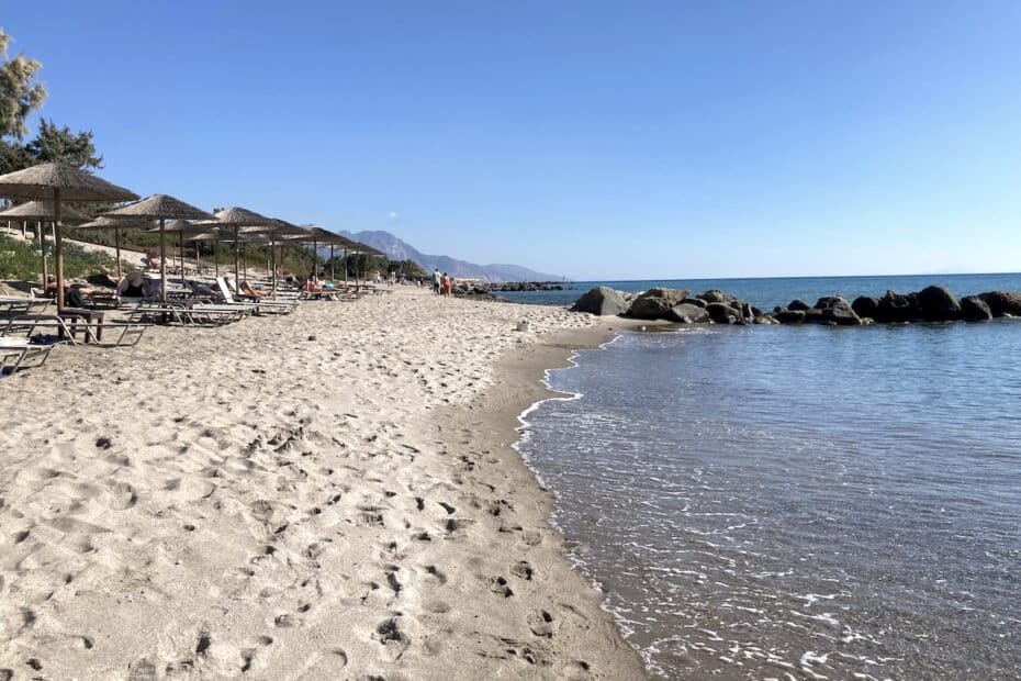 Sandstrand mit Liegen und Sonnenschirmen entlang der Küste und ruhigem Wasser.