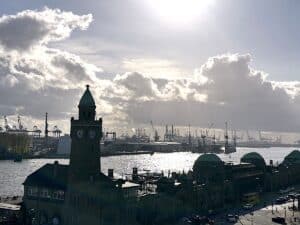 Blick auf den Hamburger Hafen mit einem Uhrturm im Vordergrund und Kränen im Hintergrund.
