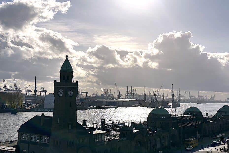 Blick auf den Hamburger Hafen mit einem Uhrturm im Vordergrund und Kränen im Hintergrund.