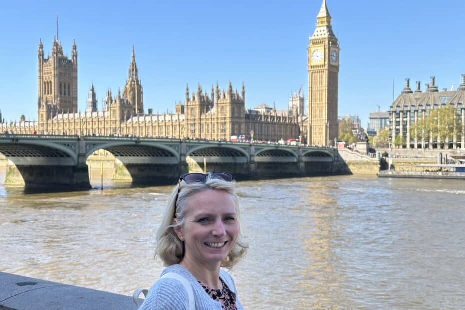 Frau mit blonden Haaren steht vor der Westminster-Brücke und dem Big Ben in London.