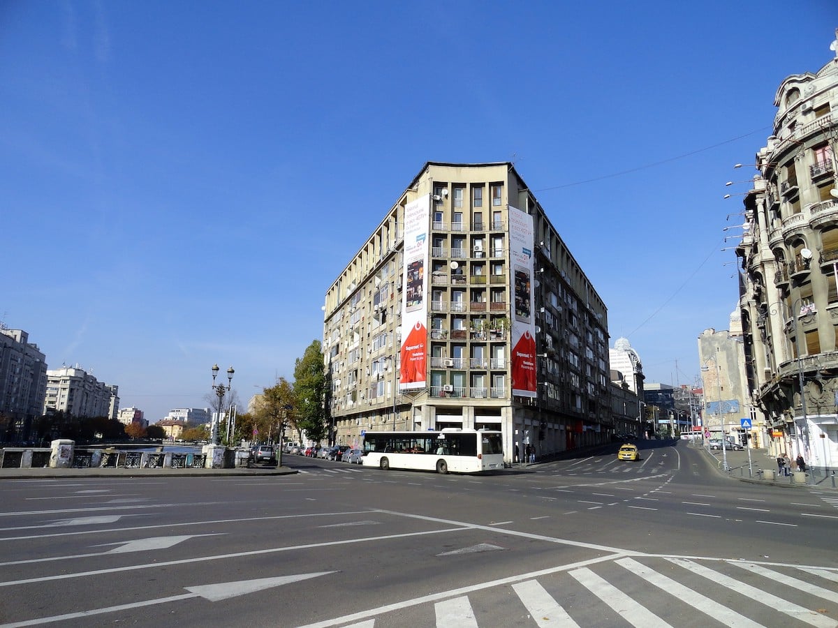 Eckgebäude mit Werbeplakaten in einer städtischen Umgebung unter blauem Himmel.