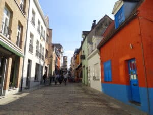 Bunte Häuser in einer gepflasterten Gasse mit Menschen, die vorbeigehen.