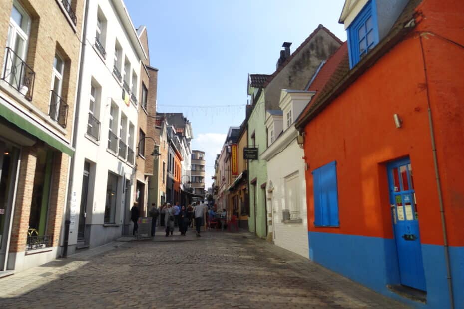 Bunte Häuser in einer gepflasterten Gasse mit Menschen, die vorbeigehen.