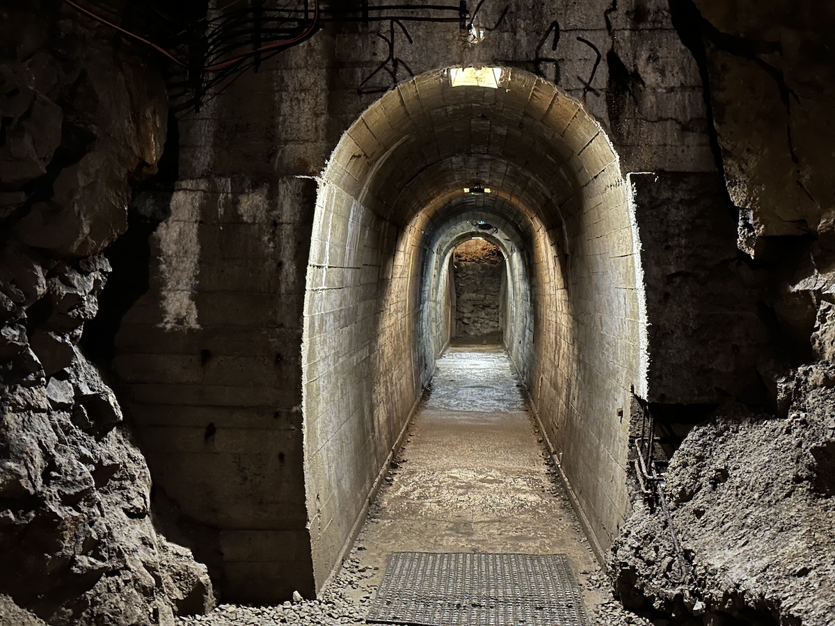 Ein beleuchteter unterirdischer Tunnel unter Schloss Fürstenstein führt durch gemauerte Bögen tief in den Felsen.