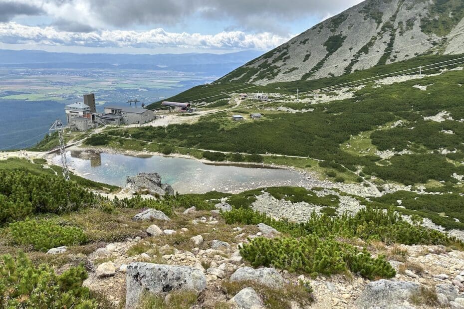 Berglandschaft mit einer Wasserfläche und einer Seilbahnstation im Hintergrund.