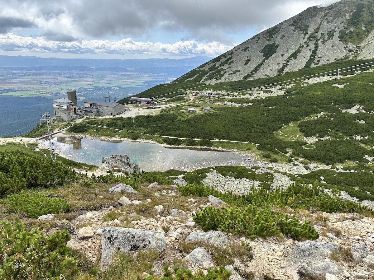 Berglandschaft mit einer Wasserfläche und einer Seilbahnstation im Hintergrund.