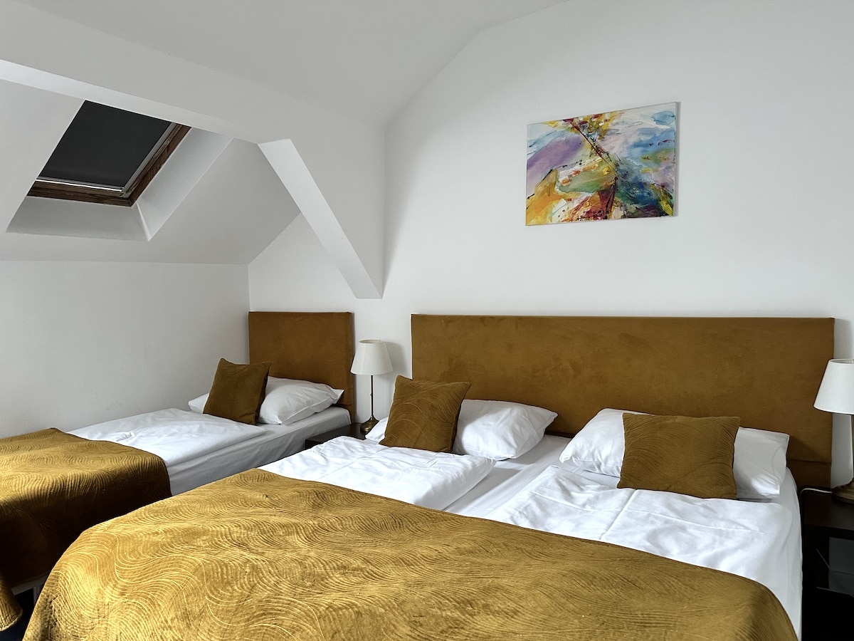 Zwei Einzelbetten mit goldfarbenen Bettüberwürfen in einem hellen Zimmer mit einem Kunstwerk an der Wand.
