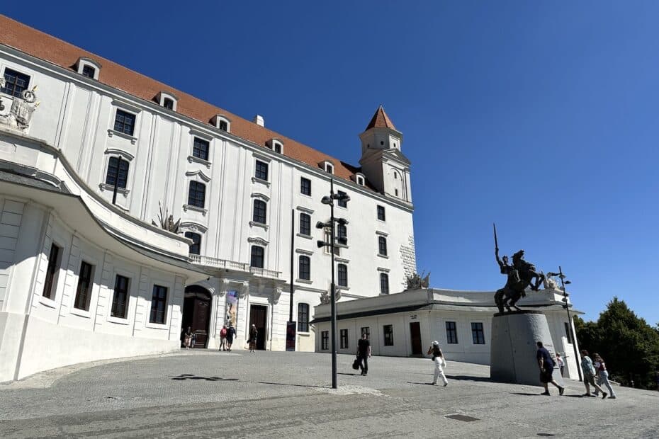 Burg Bratislava mit einer Reiterstatue im Vordergrund und blauem Himmel.