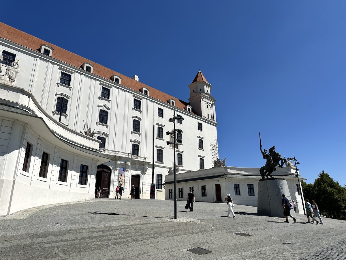 Burg Bratislava mit einer Reiterstatue im Vordergrund und blauem Himmel.