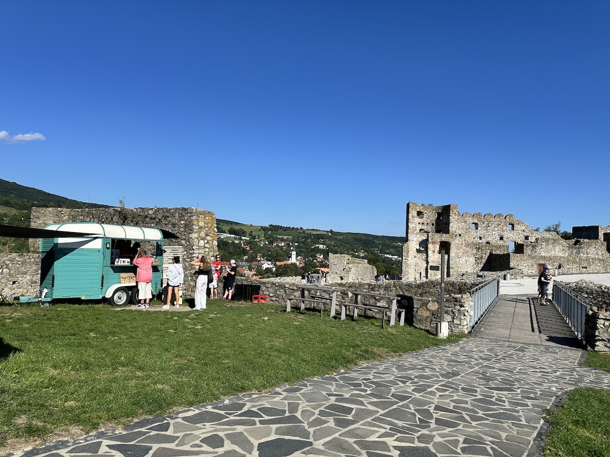 Ein mobiler Essenstand in der Nähe einer Burgruine mit Besuchern im Freien.