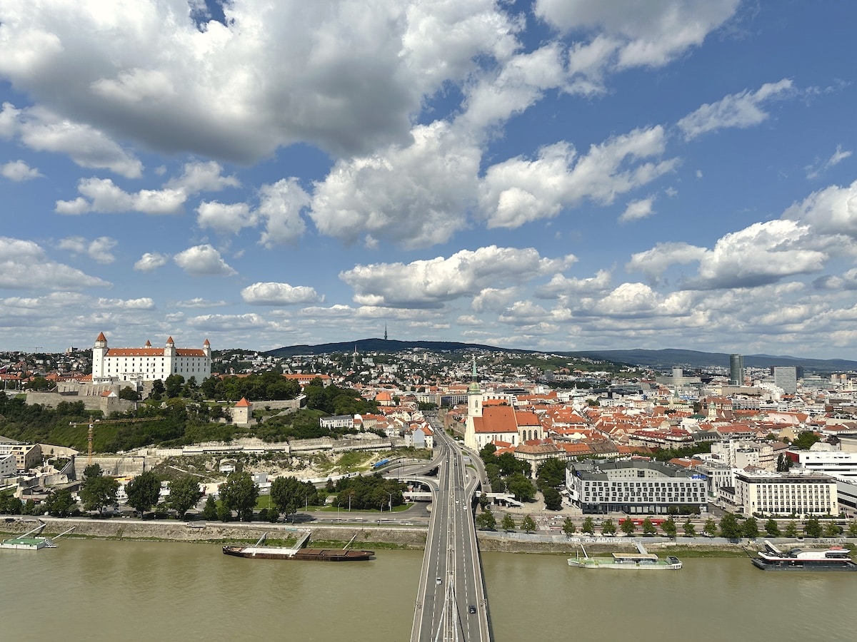 Panoramablick auf Bratislava mit der Burg und der Donau unter einem bewölkten Himmel.