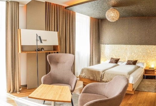 Hotelzimmer mit zwei Einzelbetten, einem Tisch und zwei Sessel in neutralen Farben.