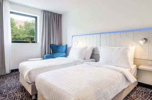 Zwei Einzelbetten mit weißen Bettwäsche in einem modernen Hotelzimmer mit Fenster.