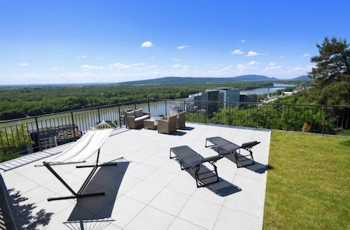 Balkon mit Liegen und Blick auf eine grüne Landschaft und einen Fluss im Hintergrund.