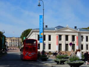 Roter Doppeldeckerbus auf einer Straße vor einem historischen Gebäude mit Fahnen.