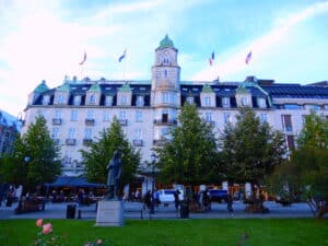 Historisches Gebäude mit grüner Dachkonstruktion und Statue auf dem Platz davor.