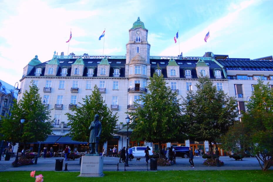 Historisches Gebäude mit grüner Dachkonstruktion und Statue auf dem Platz davor.