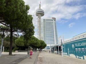 Hochhaus mit einem Aussichtsturm in Lissabon, umgeben von Bäumen und einem Gehweg.