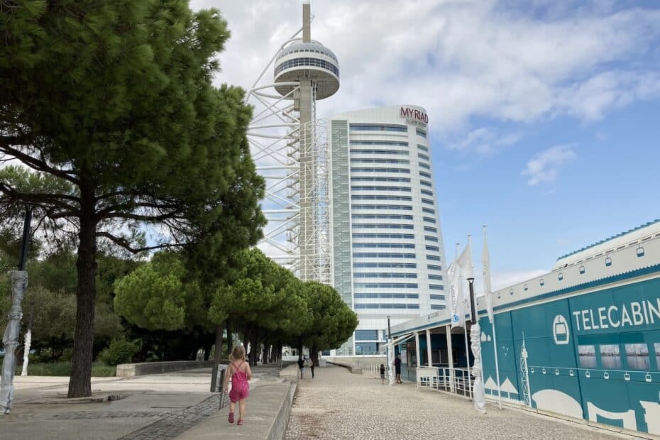 Hochhaus mit einem Aussichtsturm in Lissabon, umgeben von Bäumen und einem Gehweg.