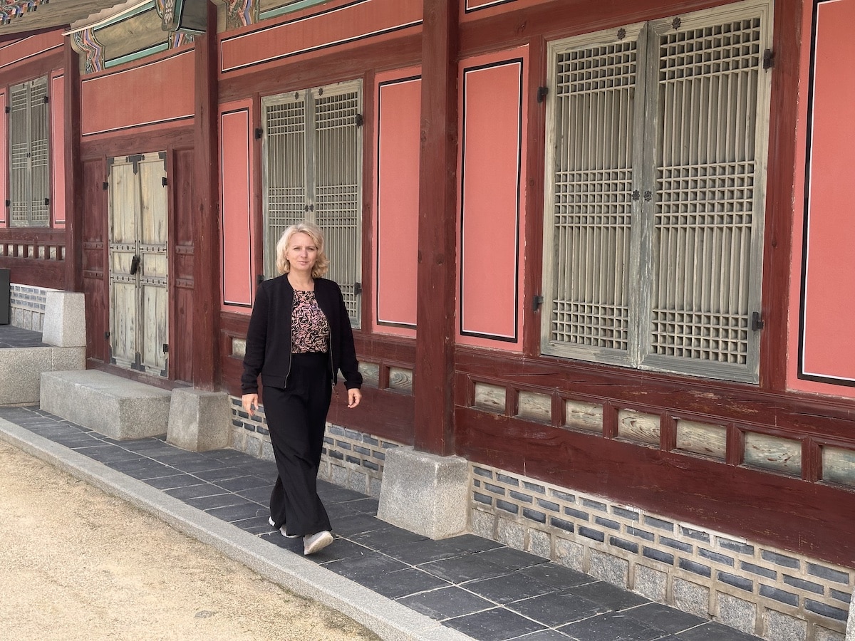 Frau in schwarzer Kleidung, die an einem roten und grauen traditionellen Gebäude entlanggeht.